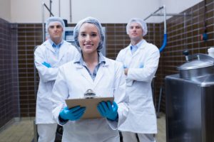 Girl holding a clipboard with these colleagues behind her in the factory