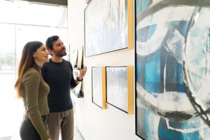 Two people discussing art pieces on a wall.