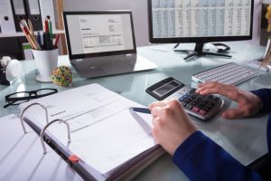 Cropped image of someone's hands doing calculations with a binder of papers beside them.