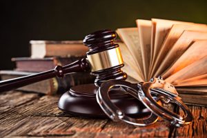 A gavel and a pair of handcuffs are lying beside an open book.