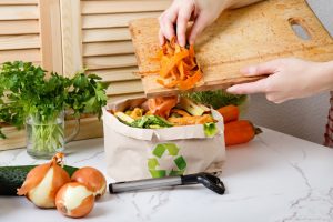 A person is scrapping food waste off of a cutting board into a recycling bag.
