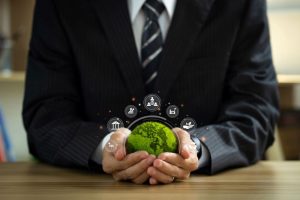 A business associate is holding a green model of earth that has different icons hovering above it.