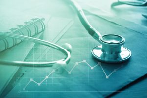 A stethoscope is laying on top of papers. There is a digital icon of a chart in front of the stethoscope.