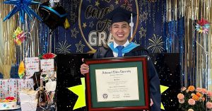 Yee Tran in cap and gown holding his JWU MBA - Hospitality Diploma.