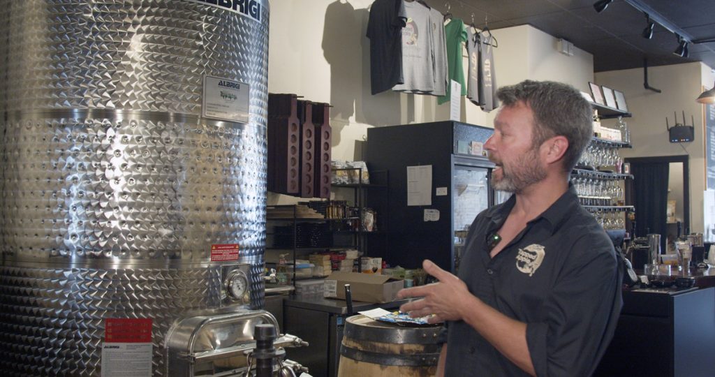 Jay Wiedenheft talking as he faces a cider-making tank that has a pressure gauge.