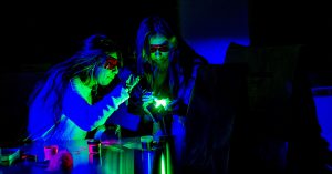 Two students in a darkened lab wearing forensic eyewear while viewing evidence with a UV light.