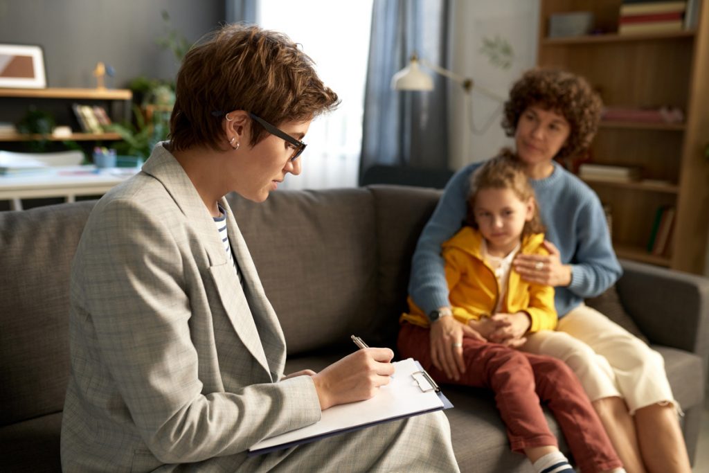 Female casework with a clipboard on her lap while interviewing a woman holding her daughter on her lap.