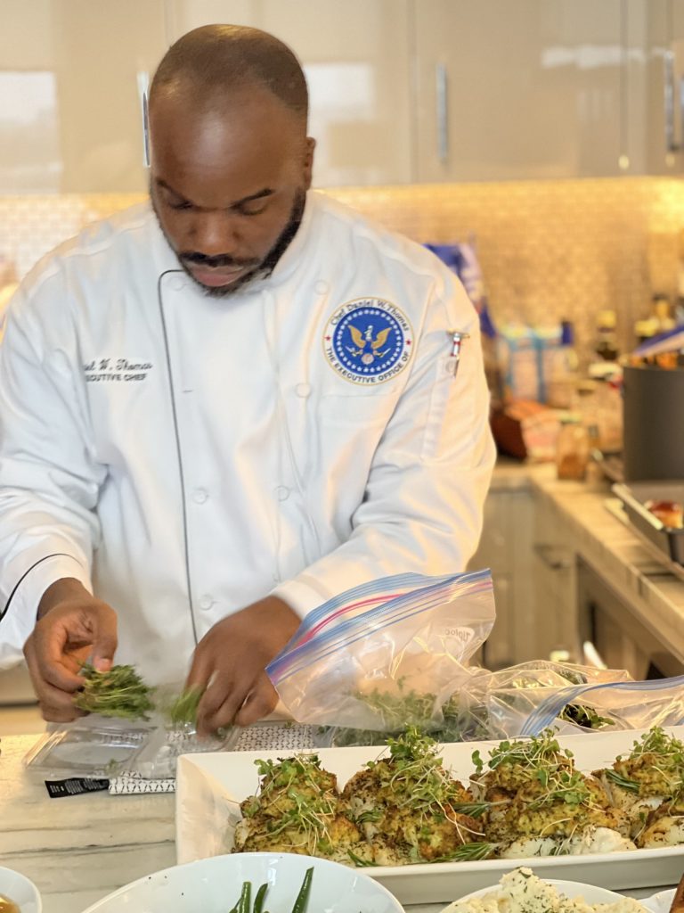 Daniel Thomas wearing chef's uniform while looking down at food he is prepping,