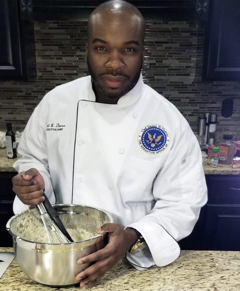 Daniel Thomas wearing white chef's uniform while whisking mixture in a stainless steel bowl.