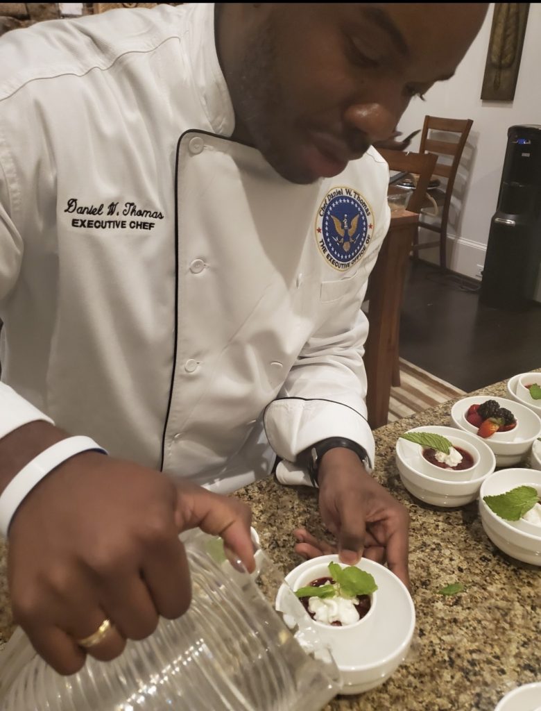 Side shot of Daniel Thomas in unform preparing a dessert.