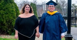 Bessie Sianis in a black dress and Demetri Sianis in his cap and gown standing together outdoors.