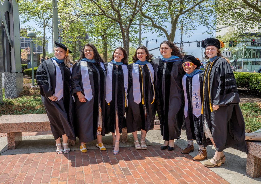 Group shot of seven graduate students of mixed gender at the War Memorial across from the Amica Mutual Pavilion following the morning 2025 Johnson & Wales Commencement in Providence.
