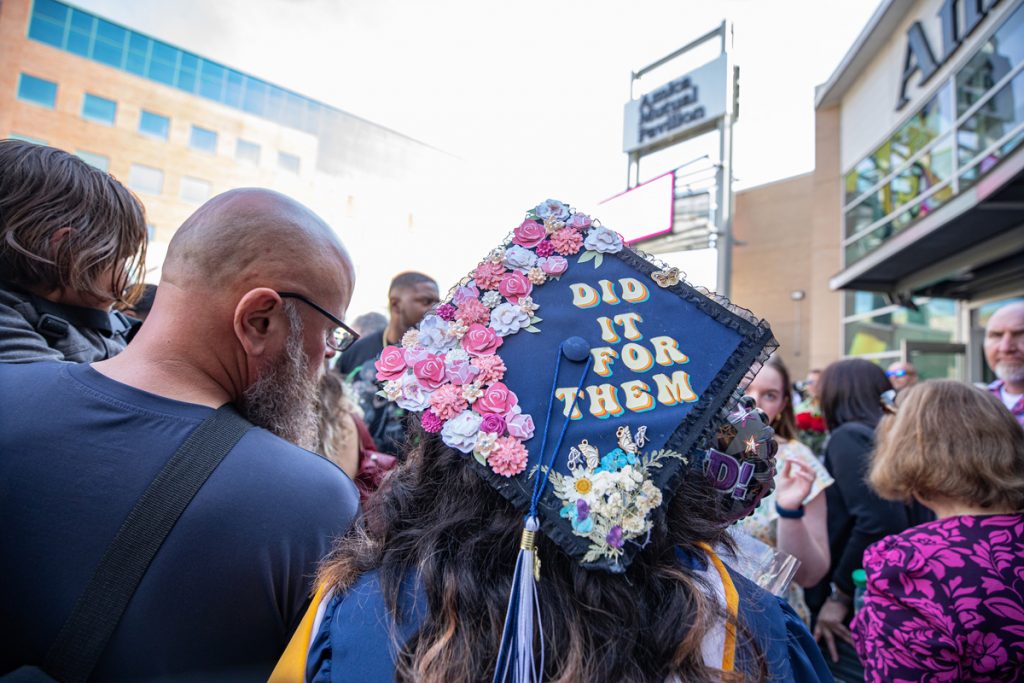 Crowd outside the Amica Mutual Pavilion featuring a graduation cap adorned with flowers and the words, "I did it for them," following the 2025 Johnson & Wales Commencement ceremony in Providence.