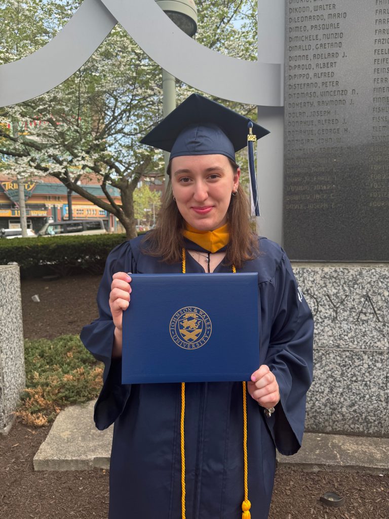 Smiling female, Chloe LaSalle, holding the diploma she received in the 2025 Johnson & Wales Commencement ceremony in Providence.