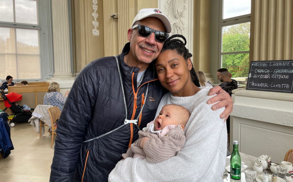 African American man in his fifties with his arm around his daughter, who holds her baby daughter.