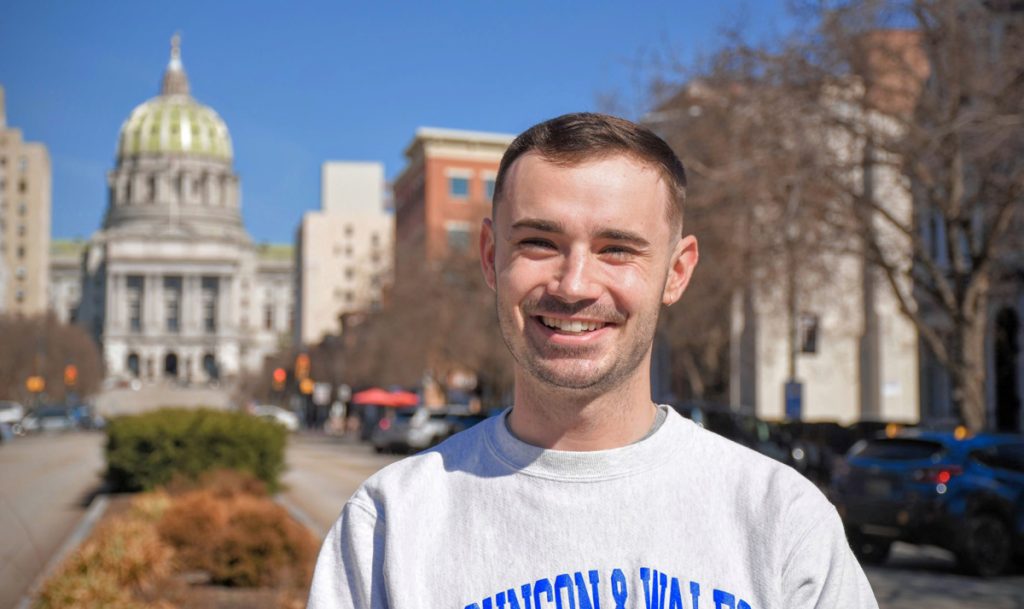 Young man, Ben, smiling, with the State Capitol Building in Harrisburg, Pennsylvania in the background.