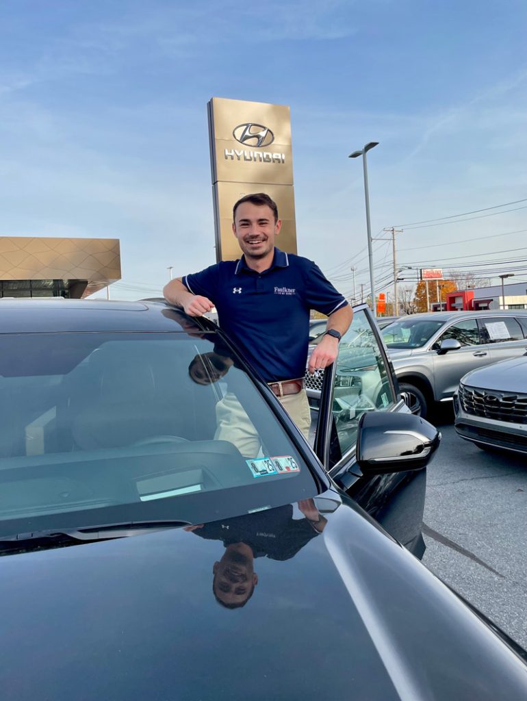 Young man, Ben. standing in a car lot with a Hyundai sign in the background.