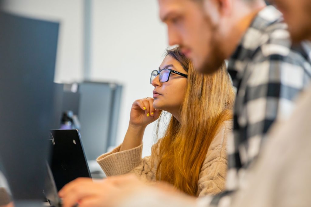 Young male and young woman appearing deep in though while viewing desktop screens.