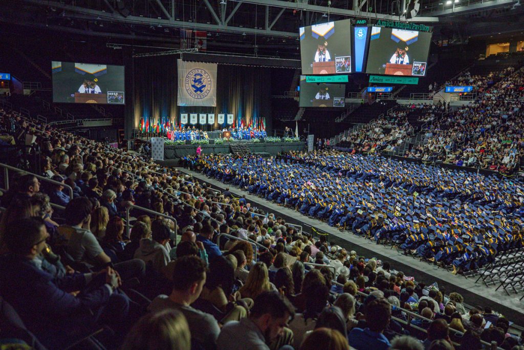 View of the Providence Commencement Ceremony in the Amica auditorium. showing the audience. seated students, the stage and on the tv screens, President. Marie Bernardo-Sousa.