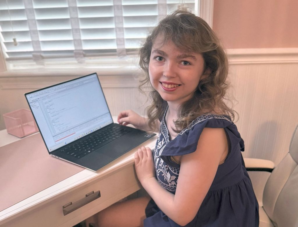 Katherine Campbell facing the camera while seated at her home desk with a laptop.
