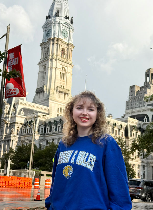 Katherine Campbell wearing her blue Johnson & Wales sweatshirt with Philadelphia, PA City Hall in the background.