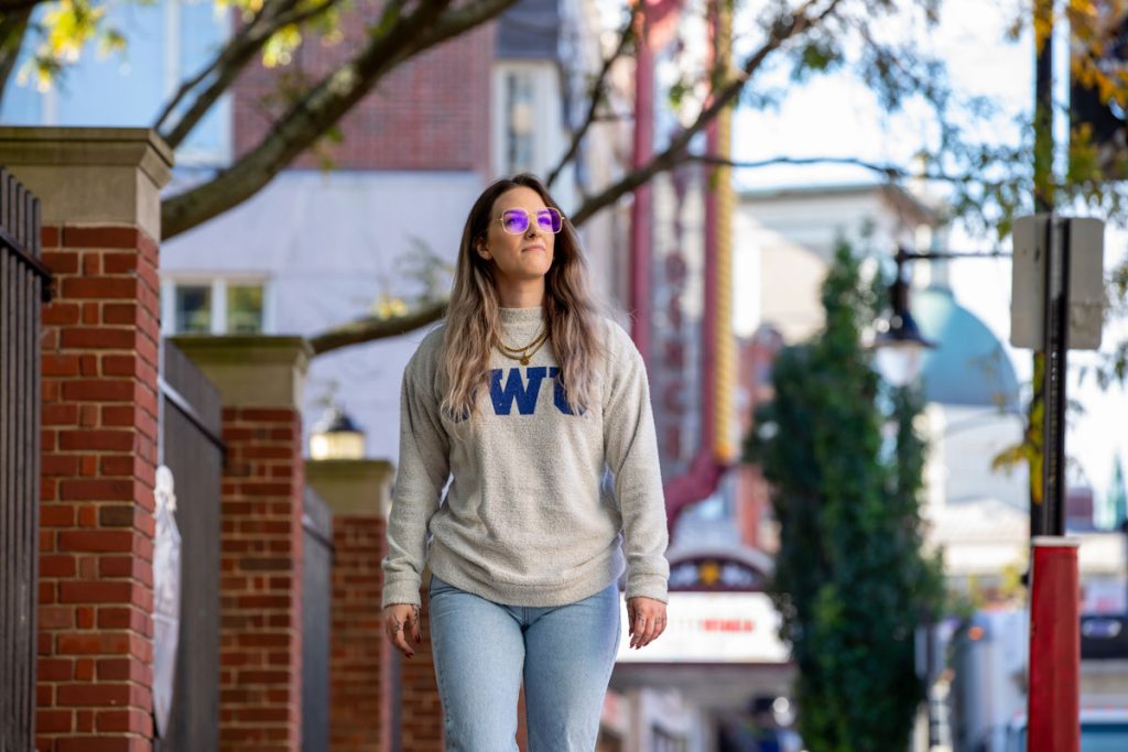 Young woman wearing a JWU sweatshirt walking through the Providence Downcity campus on a beautiful day.