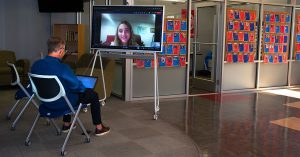 Dr. Jeff Binczyk sitting in front of a large screen displaying student, Nicole Ferraro, during a coaching and mentoring meeting,