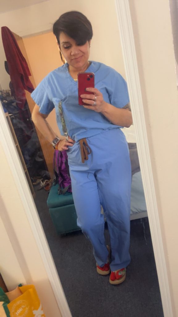 Young woman, Reyna Salcedo, in blue medical scrubs taking a "selfie" with her phone.