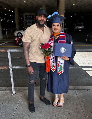 Reyna in cap and gown, holding her diploma. accompanied by her boyfriend, who supported her during her program and internship.