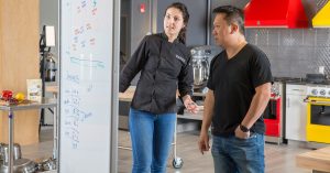 Young female student and male instructor looking at notes on a whiteboard in the Ecolab kitchen.
