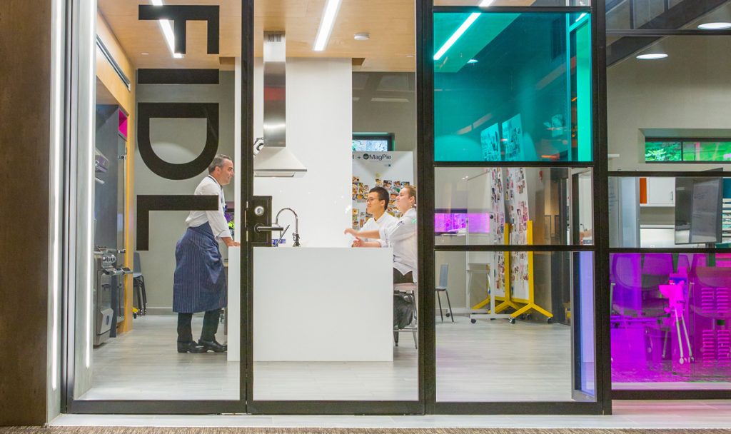 Looking through the glass panels of JWU's Ecolab Center for Culinary Science at a Professor talking with students.