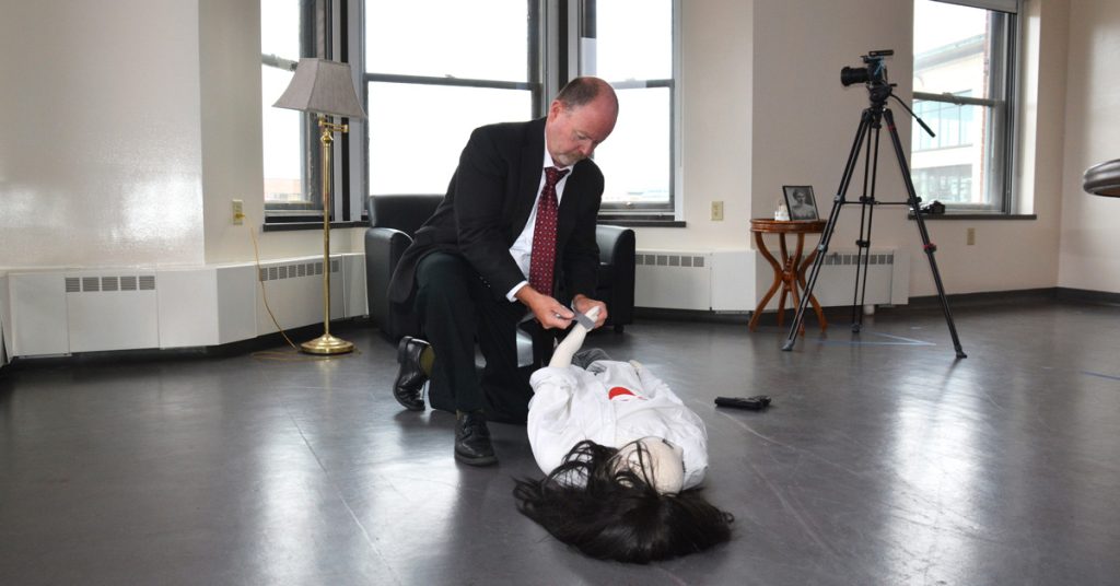 Professor James Desmarais is kneeling on the floor as he preps the dummy that will portray the victim in a crime scene.