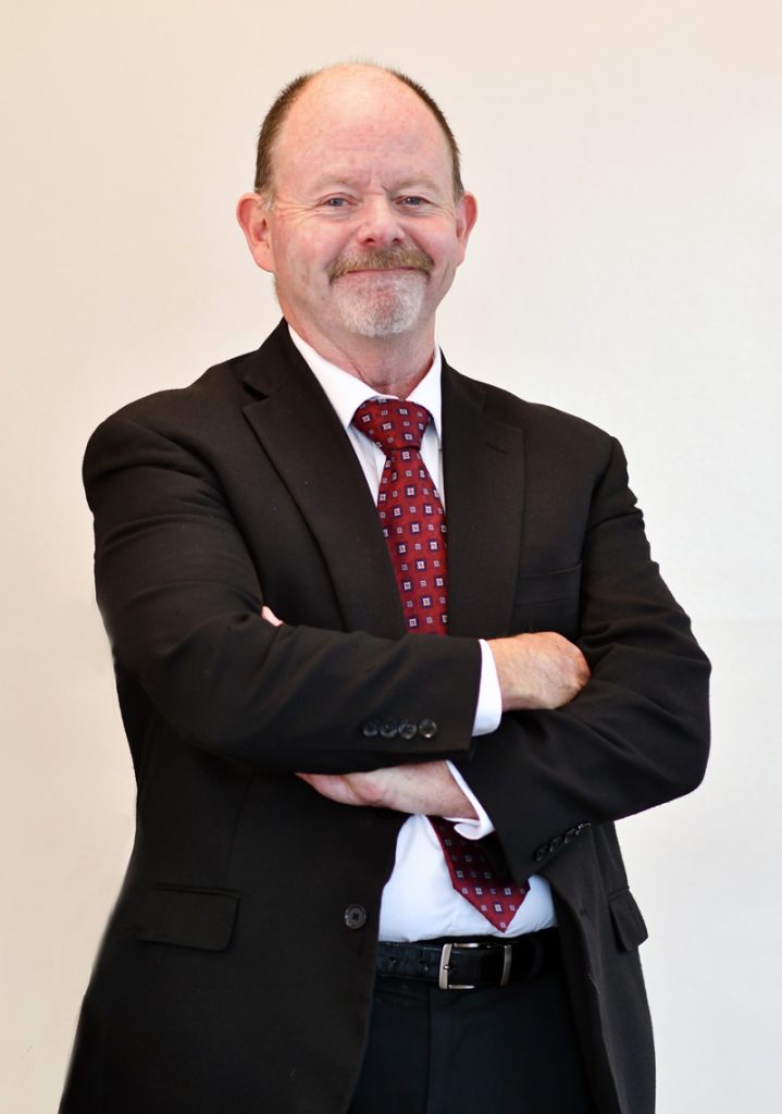 James Desmarais, male professor in the Criminal Justice programs, standing with arms folded across chest.