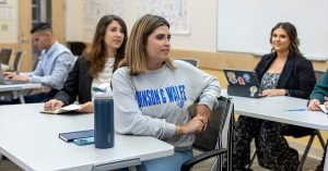 McKenzie Thibeault wearing a gray Johnson & Wales sweatshirt, seated at a table with other students in the library on the Harborside campus.