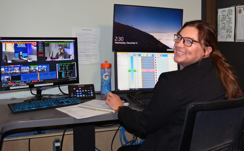 Chelsea Delfino seated in front of two computer screens, while monitoring the radio show and responding to callers at 98.5 The Sports Hub.