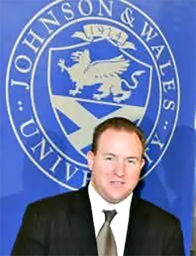 Joe Presler standing with Johnson & Wales insignia on a wall behind him at a JWU Alumni Event in Washington, D.C.