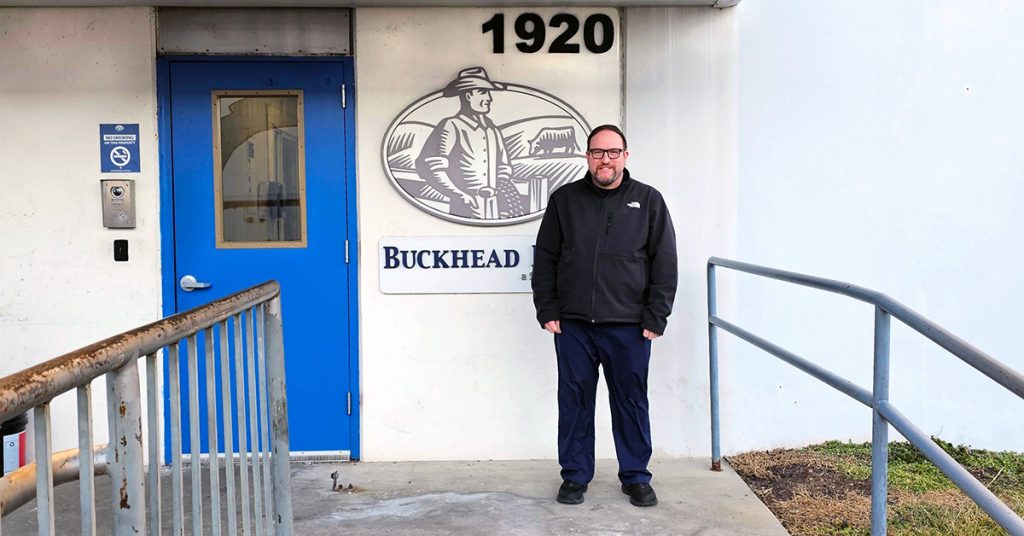 Joe Presler standing in front of a building with the logo for Buckhead, a division of  Sysco.