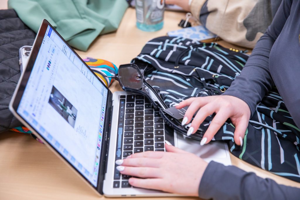 Close-up of a woman's manicured hand on a laptop keyboard while her other hand rests on a garment.
