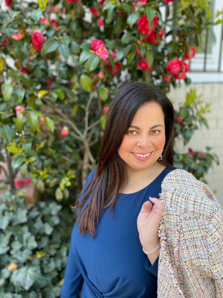 Portrait of Dr. Tamara Blake standing in front of foliage with red flowers.