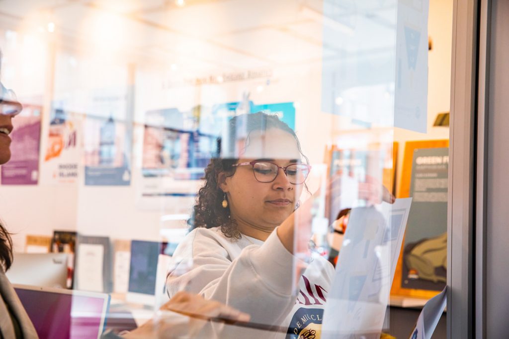 Adult female student viewed through a classroom window as she works on a design project.