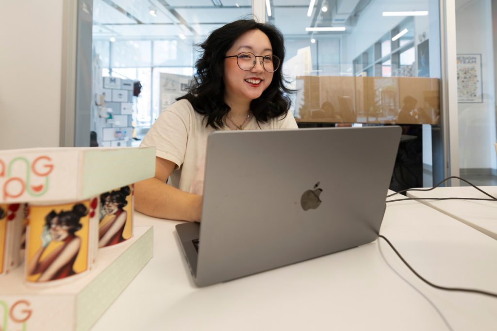 Young Asian woman wearing glasses and smiling as she works on  a laptop.