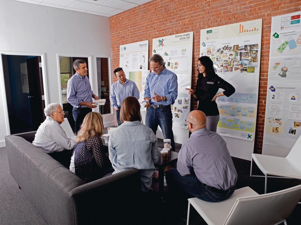 Group of adults of mixed gender, examining a product and discussing marketing.