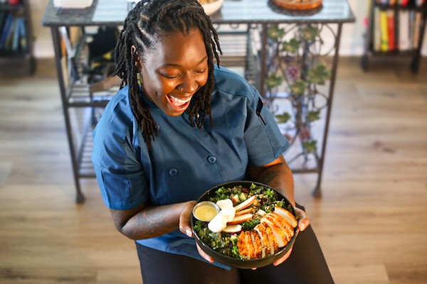 Direka Gordon seated and smiling as she looks at an artfully arranged sliced chicken salad plate she is holding.