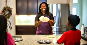 Direka Gordon in her home kitchen making pizza dough, while her son and daughter look on.