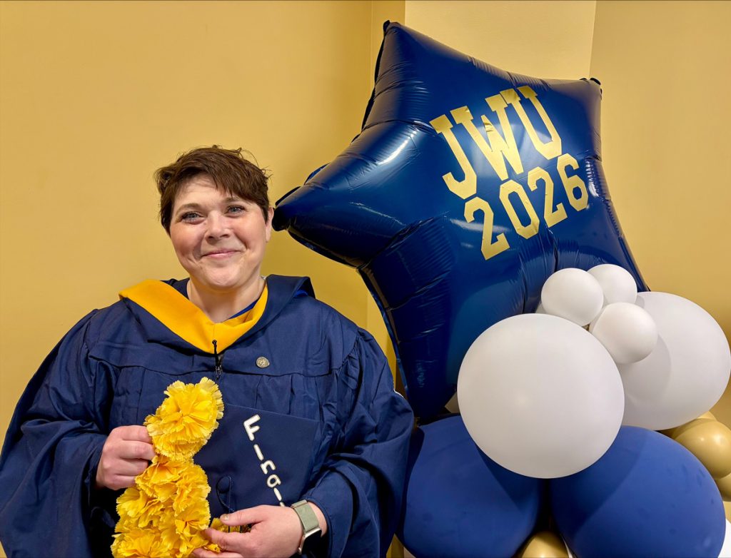 Lacey J. Meyer standing next to the blue and white balloon decoration embossed with JWU 2026 in gold letters, at the JWU Online 2026 Senior Toast held in the Wildcat Center on the afternoon before commencement.