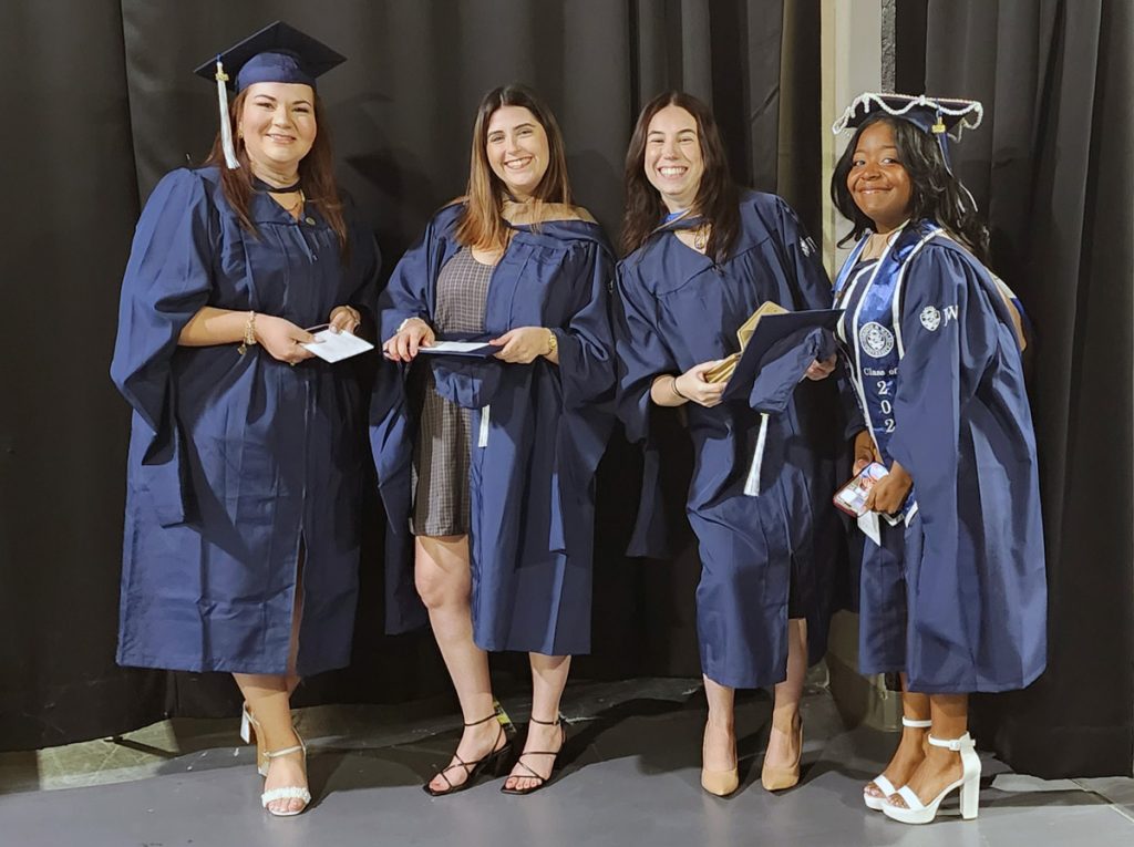 McKenzie Thibeault, second from left, in her gown and holding her cap, with three JWU friends in their caps and gowns, waiting in the tunnels before the ceremony at the Amica Mutual Pavilion.