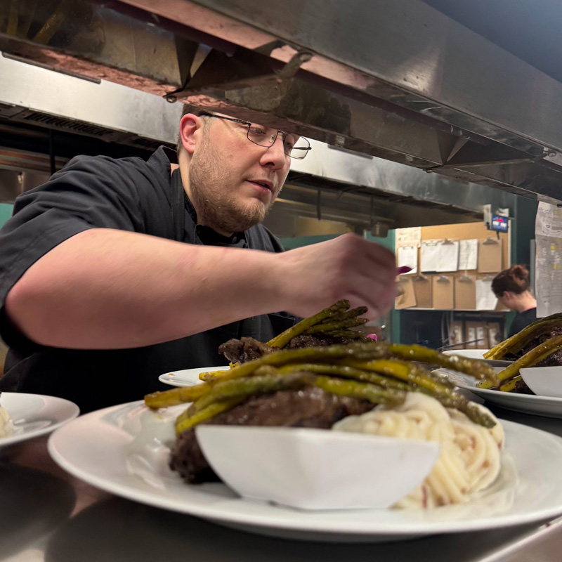 Michael Yates in the kitchen at a private club, preparing a main course dish.
