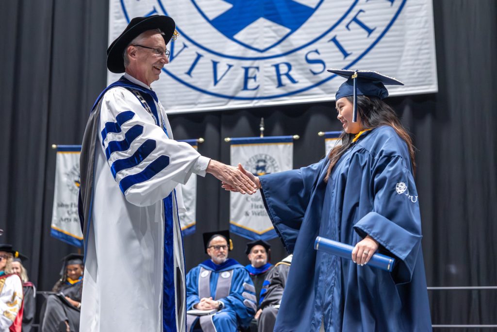 President Mathieu shaking the hand of a female graduate at the JWU Charlotte Commencement in the Bojangles Coliseum, Charlotte, North Carolina.