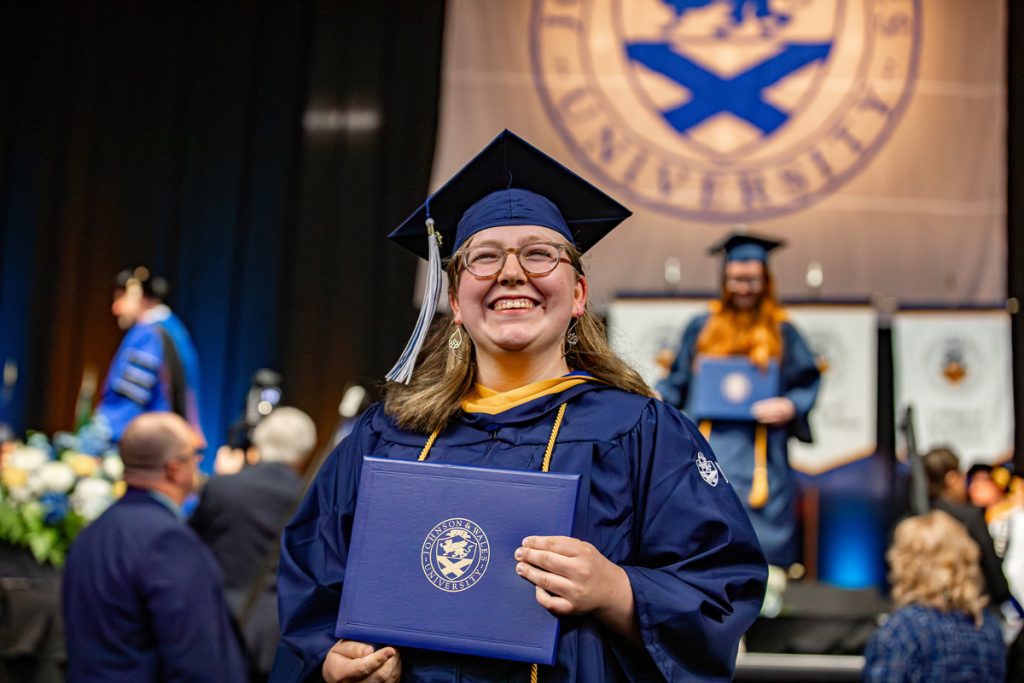 New female graduate holding her diploma smiling as she exits the stage.