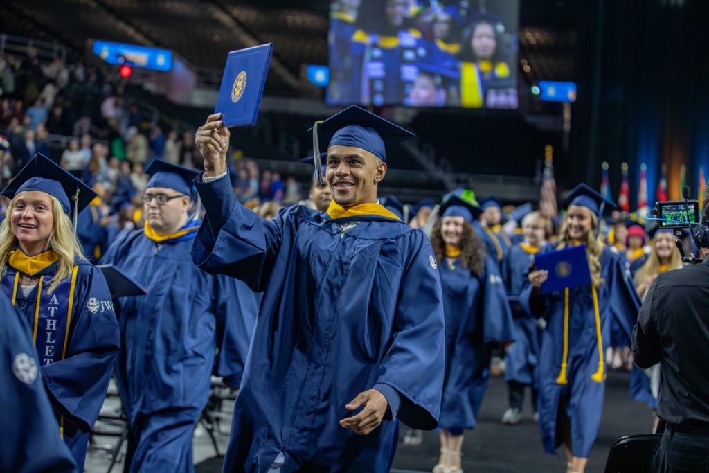 Procession of students following the commencement ceremony with one male graduate holding hid diploma over his head.
